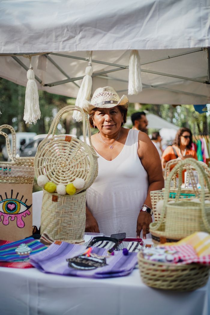 A woman vendor displays handmade crafts at an outdoor market, showcasing colorful, artisanal products.