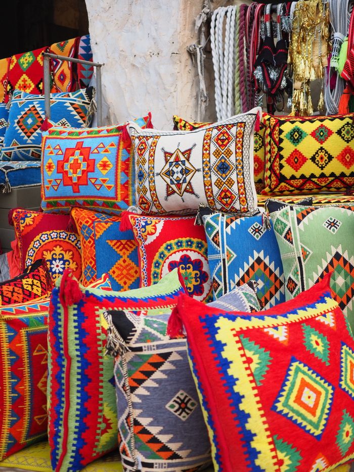 Vibrant geometric pattern cushions on display in a Doha market, showcasing traditional Middle Eastern designs.